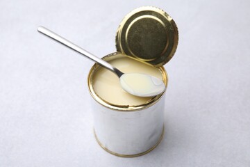 Open tin can with condensed milk and spoon on white table