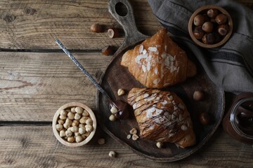 Delicious croissants with chocolate and nuts on wooden table, flat lay