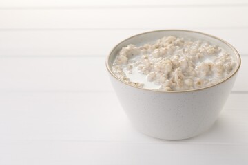 Tasty boiled oatmeal in bowl on white wooden table, closeup. Space for text