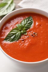 Delicious tomato soup with basil and spices on table, closeup