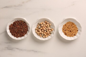 Growing microgreens. Different seeds in bowls on white marble table, flat lay