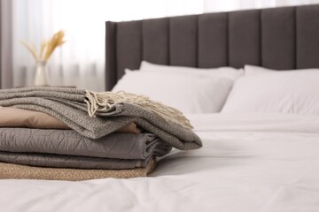 Stack of different folded blankets on bed in room, space for text. Home textile