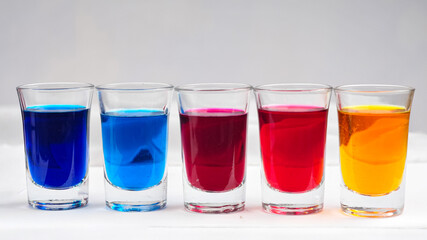 Small glasses filled with colorful water are neatly arranged on an isolated white background