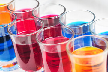 Small glasses filled with colorful water are neatly arranged on an isolated white background
