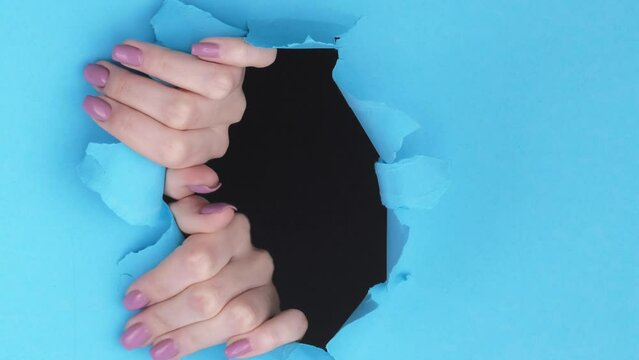 Vertical video. Breakthrough paper hands in hole. Curious female fingers touching ripped wall rough edge commercial background with empty space.