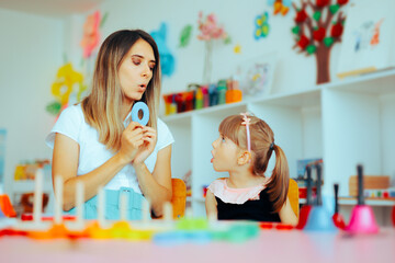 Speech Therapist Teaching Child How to Pronounce the Letter O. Child suffering from dyslexia exercising her communication skills with professional help
 - obrazy, fototapety, plakaty