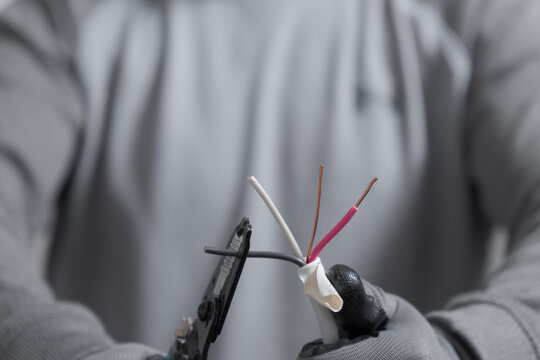 Unrecognizable electrician man wearing gloves cutting electrical cables with a tool