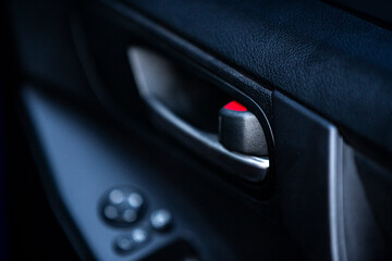 Close up of a car door handle with a red button in the car