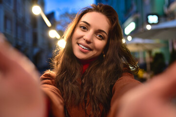 Happy elegant young woman in red coat taking selfies while walking around the city. girl hugs her boyfriend