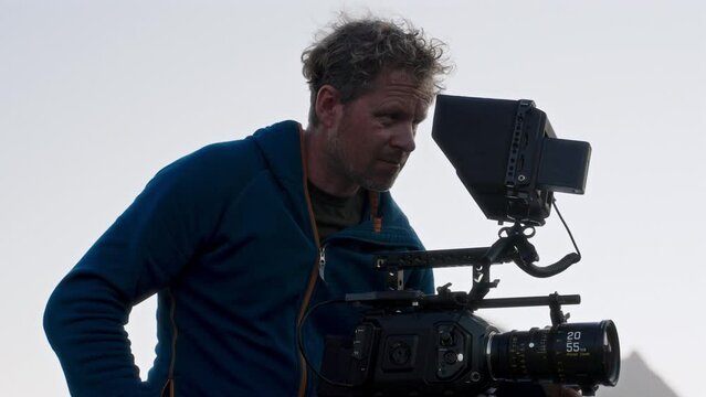 A Focused Filmmaker In Blue Jacket Filming