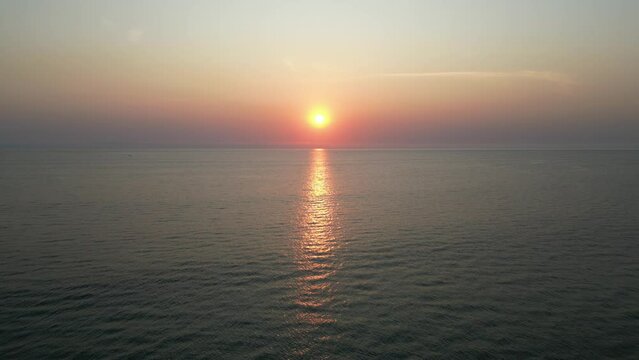 Aerial view of sunset or sunrise on the ocean with calm wave in Bali. Dusk or dawn on the beach with clear sky. Sunlight reflection on middle of the sea. Wide angle cinematic for opening ending scene.