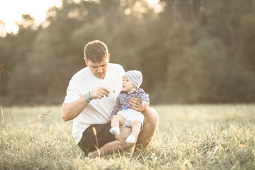 A dad  enjoys a playful moment in a summer field, as the dad  throw  baby son. The cheerful family...