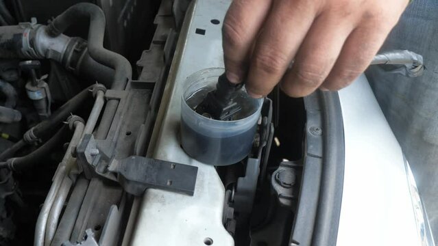 Fingers dipping a CNG or Compressed Natural Gas injector of a car engine into a container with some cleaning liquid agent.