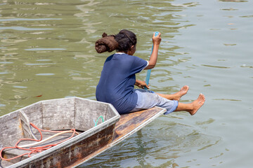 A woman sits on the prow of a boat and is paddling with a paddle, Thailand