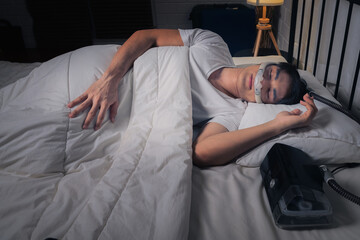 Happy and healthy Asian man with CPAP machine on side table wearing CPAP mask sleeping smoothly in bed all night without snoring