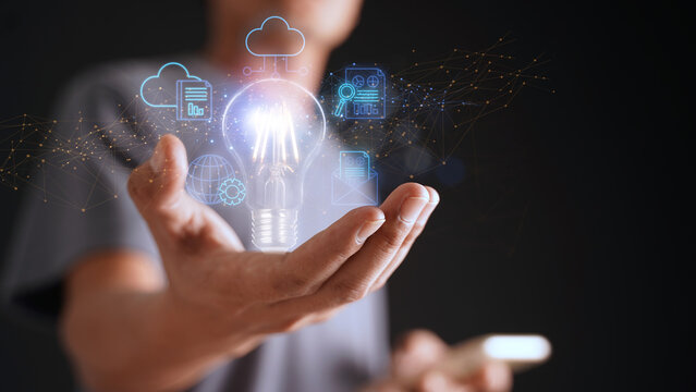An entrepreneur holding an abstract light bulb uses the internet to connect data on his mobile device through artificial intelligence. Concept of data storage, large data warehouse on cloud computing.