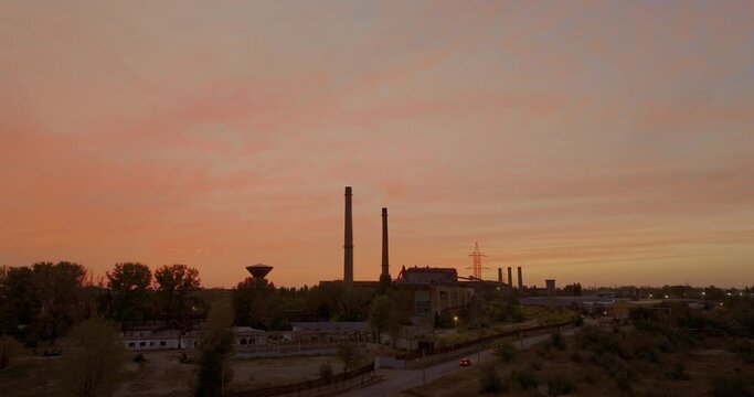 Aeria tracking shot of a warm embrace of a stunning sunset illuminates a time-worn industrial area and the silhouettes of towering furnaces stand sentinel 4K50fps cinematic grade