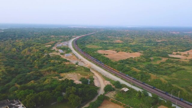 Aerial Drone shot of a Freight train moving through semi arid forest valley of Chambal river in India