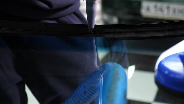 A close-up of the windshield repair process in a car service, blue professional suction cups are visible on the glass. The master applies glue.
