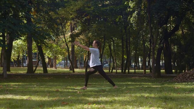 Pregnant woman stretching her arms, yoga mat, asana, yoga pose, city park green lawn trees, stretching, balance. Meditation, exercises, calmness, morning sunshine