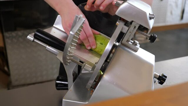 A close-up of a chef slicing zucchini into thin slices using an industrial slicer in the restaurant kitchen. 