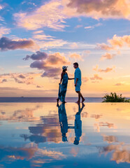 Young men and women watching the sunset with reflection in the infinity swimming pool at Saint Lucia Caribbean, couple at infinity pool during sunset at a luxury vacation