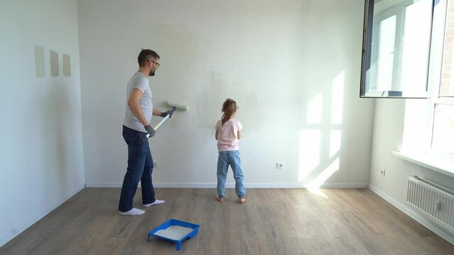 Back view father and little daughter paint wall with rollers at home in flat. Family make renovations in new apartment. Repair concept
