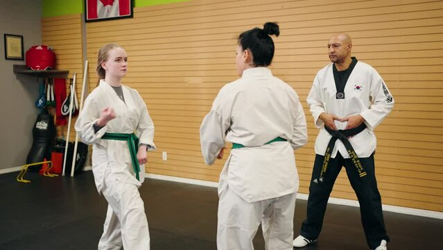 A 4K Slow Motion Young Fit Teenage Girl Mother Daughter Taps Out on Matt in Fight Combat Defense Wrestling Karate Taekwondo Competition is Helped out my Black Belt Master inside a dojo studio gym