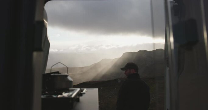 Male stand by campervan kitchen overlooking Jotunheimen sunset rainstorm