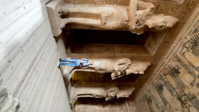Travel photographer in Egypt inside Abu Simbel Temple of Ramses II. Traveler inside temple of Abu Simbel. Tourist on a trip with camera watching statues of pharaoh Ramses II. Wanderlust, Vertical