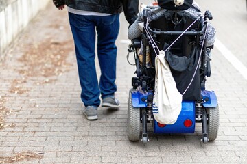 Person in a wheelchair on the street with a man beside