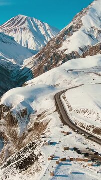 vertical Epic Aerial shot of snowy mountains with a road with cars in Georgia
