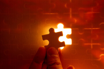 Pieces of a jigsaw puzzle filled with orange lights by hand Success concept - obrazy, fototapety, plakaty