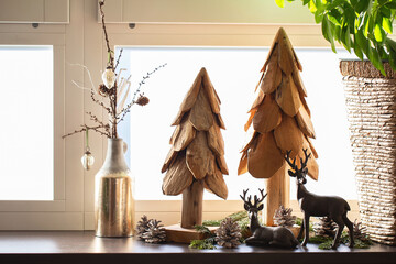 Christmas home decoration. Artificial wooden Christmas trees, fir cones and deer figurines on the...