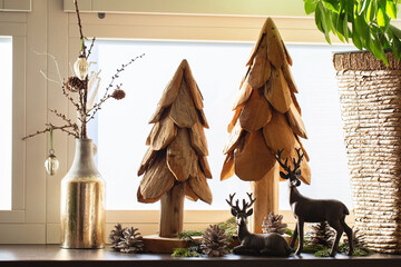 Christmas home decoration. Artificial wooden Christmas trees, fir cones and deer figurines on the...