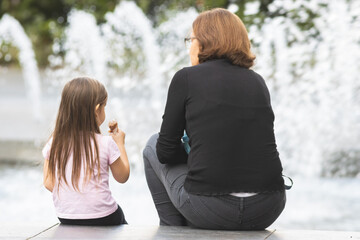 Two people -little girl and her grandmother seated, conversing and eating icecream
