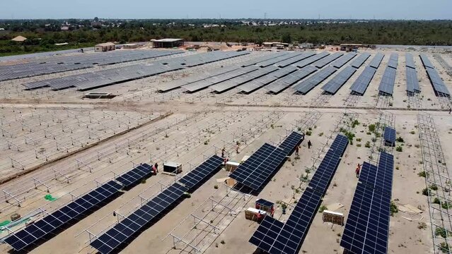 Aerial forward dolly view of technicians and engineers working installing bifacial solar panels at Jambur solar PV project site under construction in Gambia, West Africa