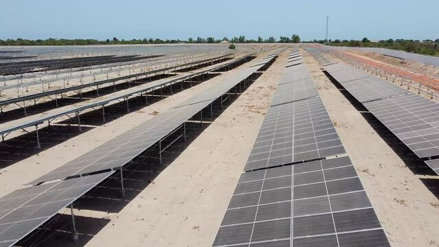 Aerial sliding left view over dirty dusty bifacial solar panels at Jambur solar energy generation project site under construction in Africa
