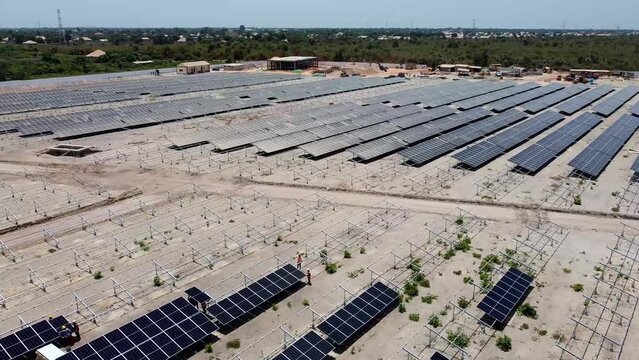 Aerial rotating dolly view of technicians and engineers working installing bifacial solar panels at solar farm project site under construction in Jambur, Gambia