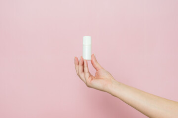 White bottle, drops for eye, nose or ear in hand on pink background. Pharmaceutical product.