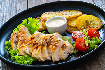 Grilled chicken breast, fried potatoes and fresh vegetables on wooden table
