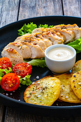 Grilled chicken breast, fried potatoes and fresh vegetables on wooden table
