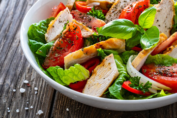 Caesar style salad - grilled chicken breast and fresh vegetables on wooden table