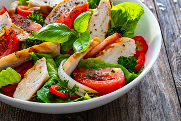 Caesar style salad - grilled chicken breast and fresh vegetables on wooden table