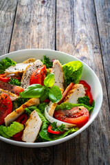 Caesar style salad - grilled chicken breast and fresh vegetables on wooden table

