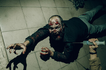 Zombie dead man creeps on floor halloween concept. Doctor with cure vaccine syringe in hand