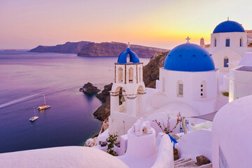 White churches an blue domes by the ocean of Oia Santorini Greece, a traditional Greek village in Santorini during summer at sunset, streets of Oia Santorini