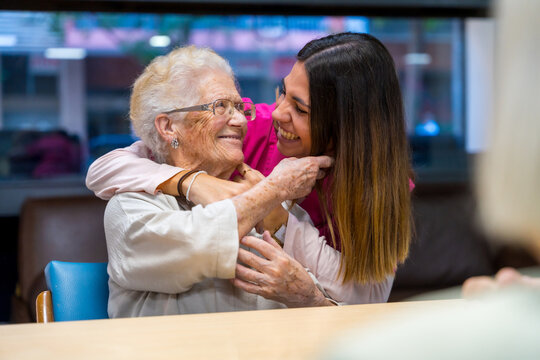 Happy elder woman and nurse embracing in a geriatric