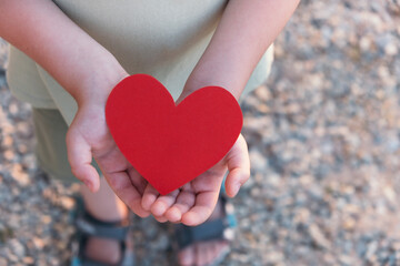 Fototapeta premium Child holding red heart. Heart health, charity and hope concept. Top view