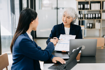 Obraz premium Asian business colleague business presents and explains and using laptop and tablet. Teamwork, financial marketing team, while sitting in modern office